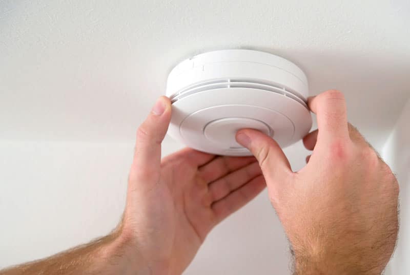KI-basierte Bildbeschreibung | Eine Person, die einen Rauchmelder an einer weißen Decke installiert oder prüft.